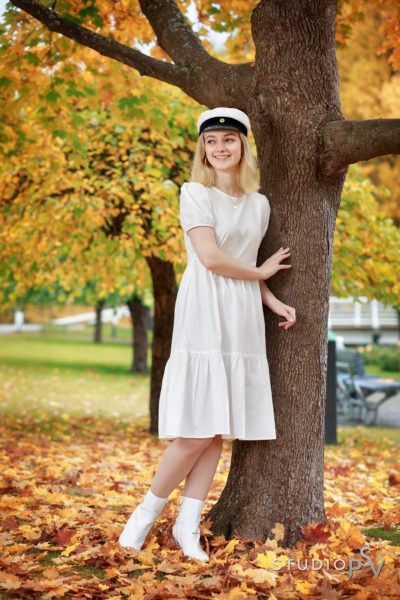 ylioppilastyttö nojaa puuhun ruskaisessa Ainolan puistossa