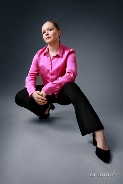 Nuori tyylikäs nainen pinkissä paidassa ja mustissa pitkissähousuissa Studio P.S.V:n promokuvassa