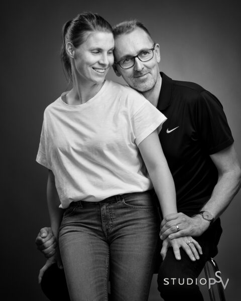 Keski-ikäinen pariskunta sylikkäim Studio P.S.V:n mustavalkoisessa muotokuvassa iloisella meinigillä.