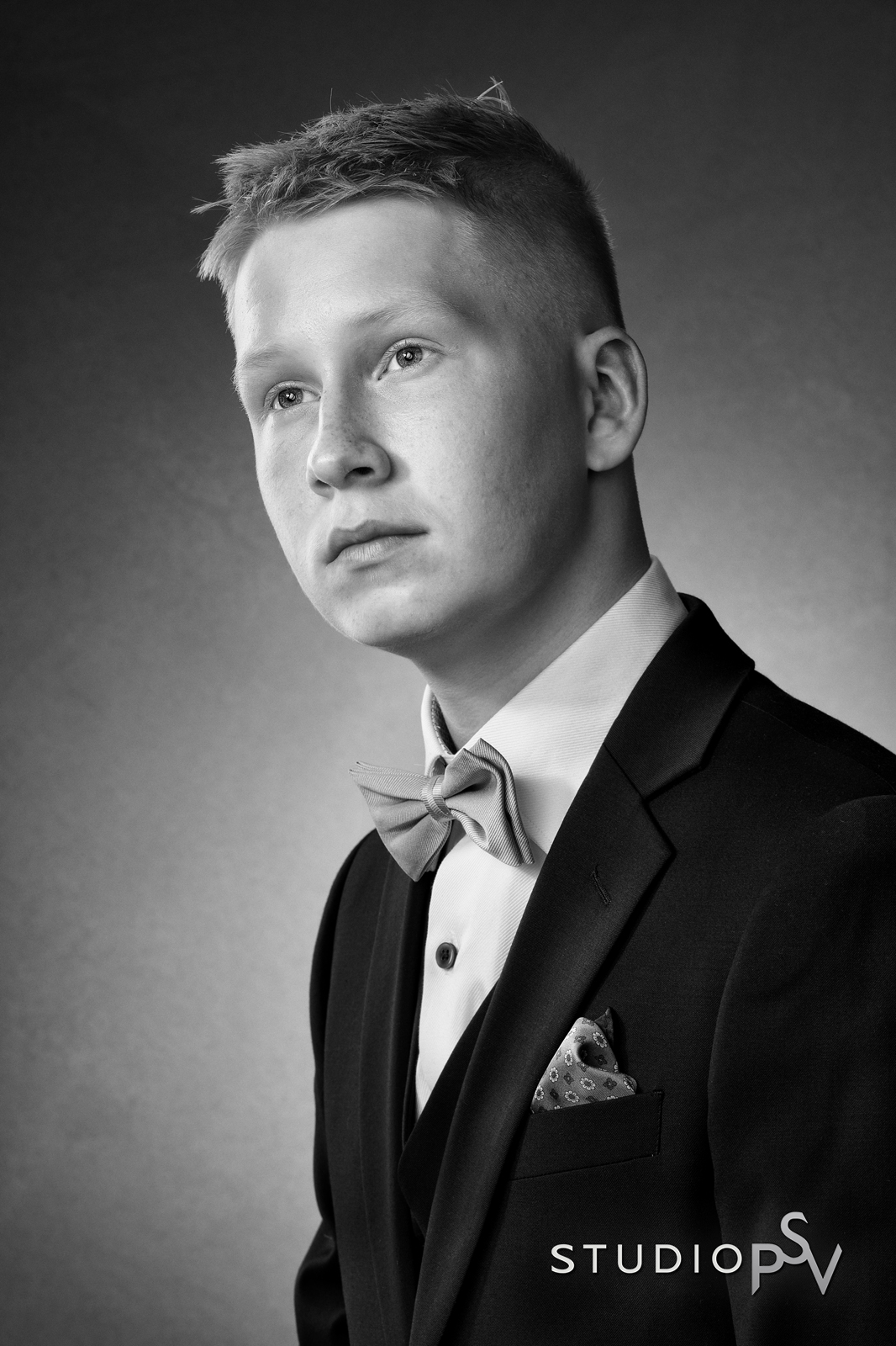 Nuori poika mustavalkoisessa rippikuvassa katsoo totisena kameran ohi.