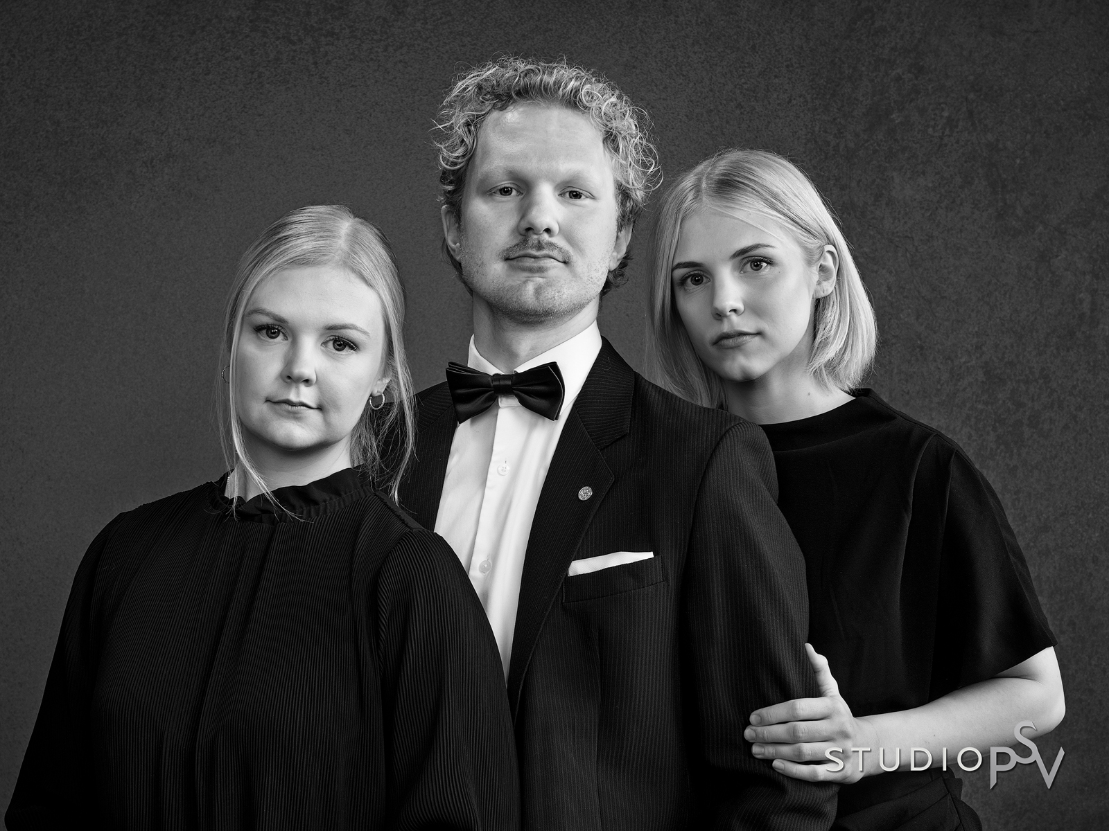 Kolme aikuista sisarusta, kaksi tyttöä ja poika, katsovat kameraan mustavalkokuvassa.