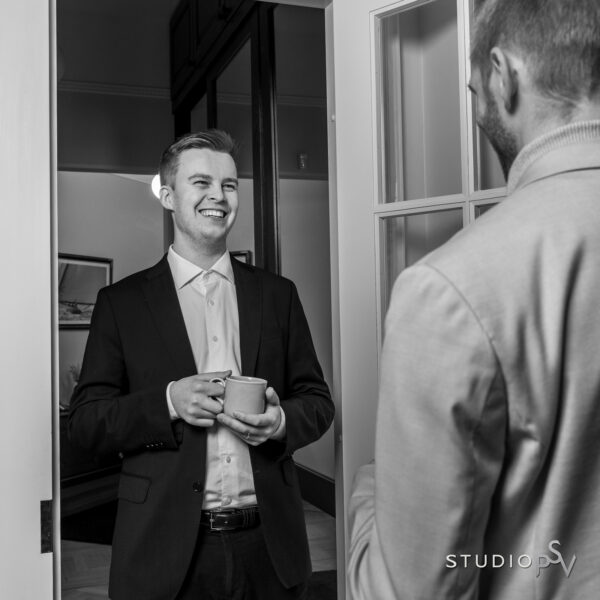 Nuori mies kahvikuppi kädessään juttelee kuvassa selin olevan henkilön kanssa.